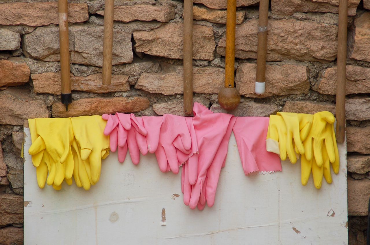 Pink and yellow rubber gloves hanging on a rustic brick wall, perfect for gardening and housework.