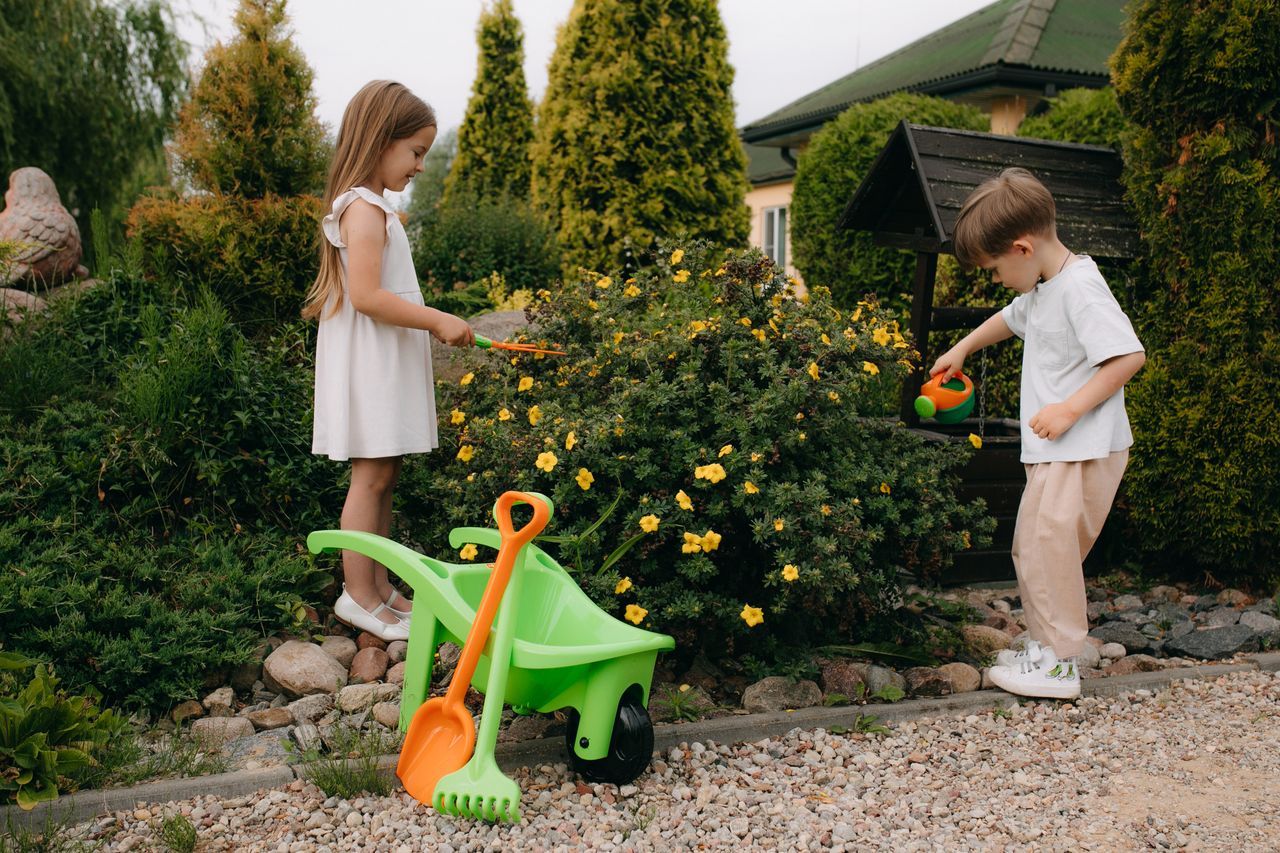 Kids playing with gardening tools among blooming flowers in a vibrant backyard setting.